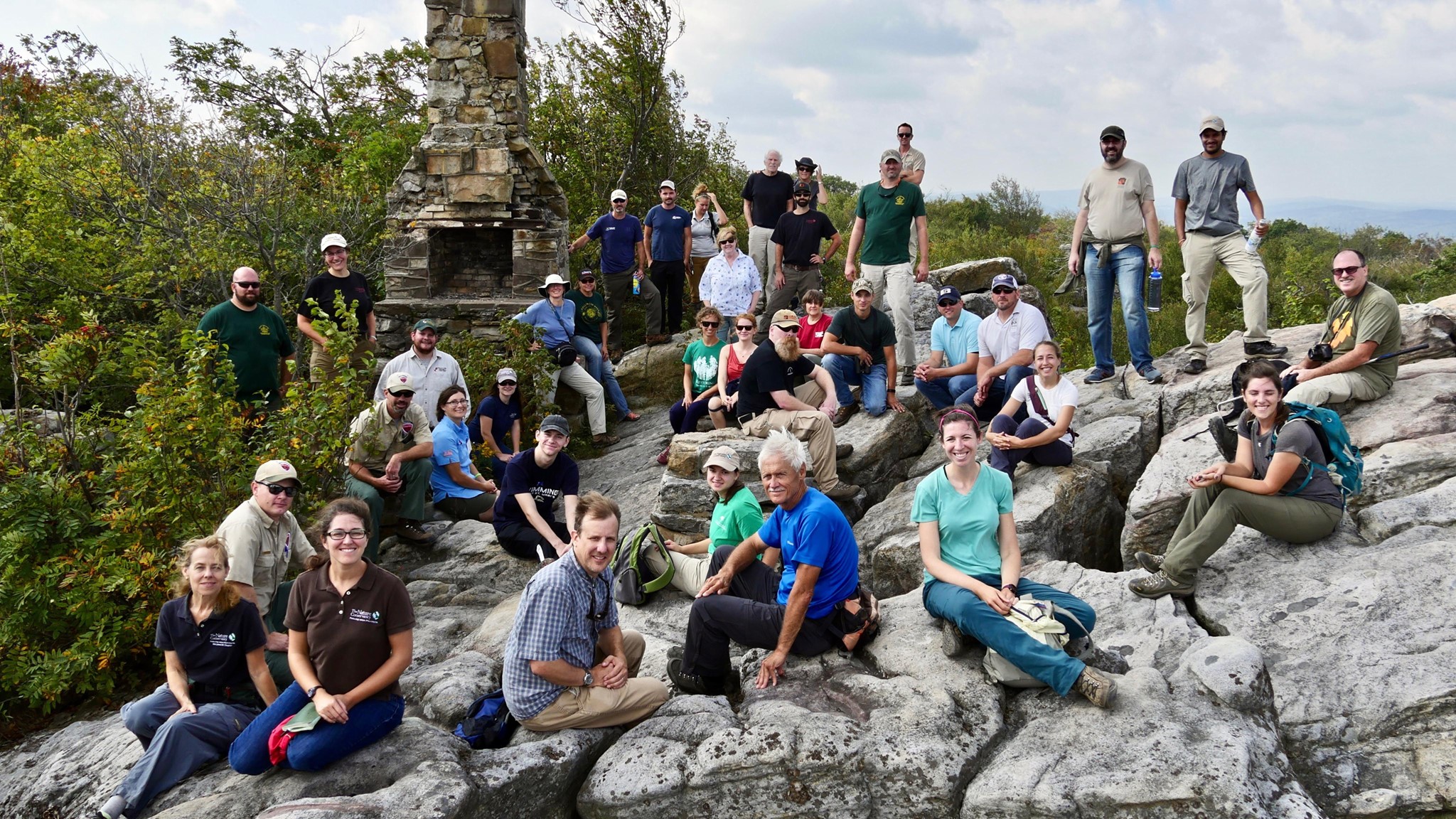 A large group of people pose while standing and sitting on an outcropping of rock.