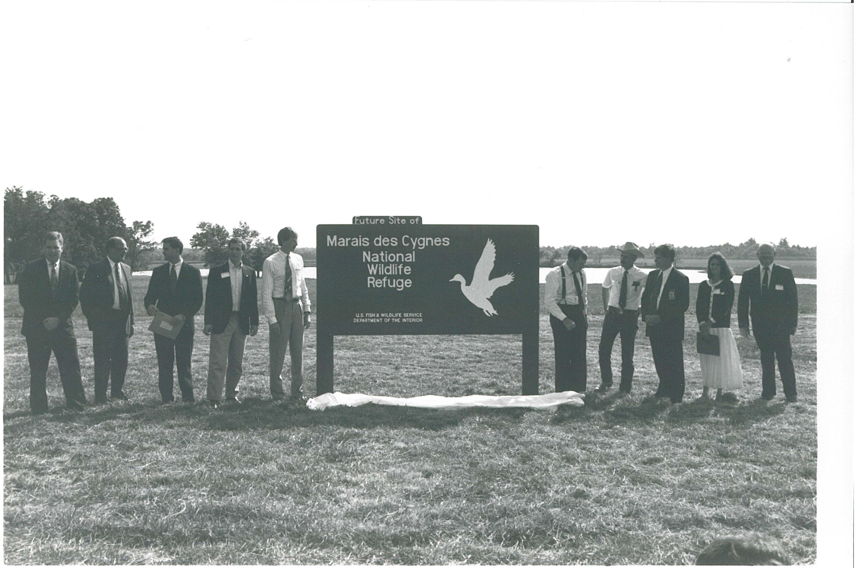 Nine men and 1 woman stands next to entrance sign.