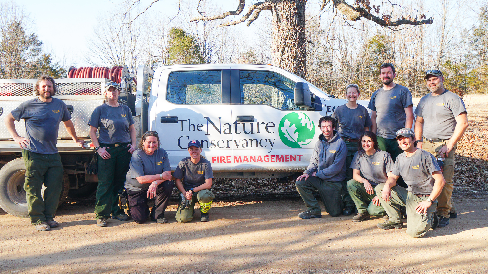 A group of people posing for a photo in front of a white TNC fire management truck. 