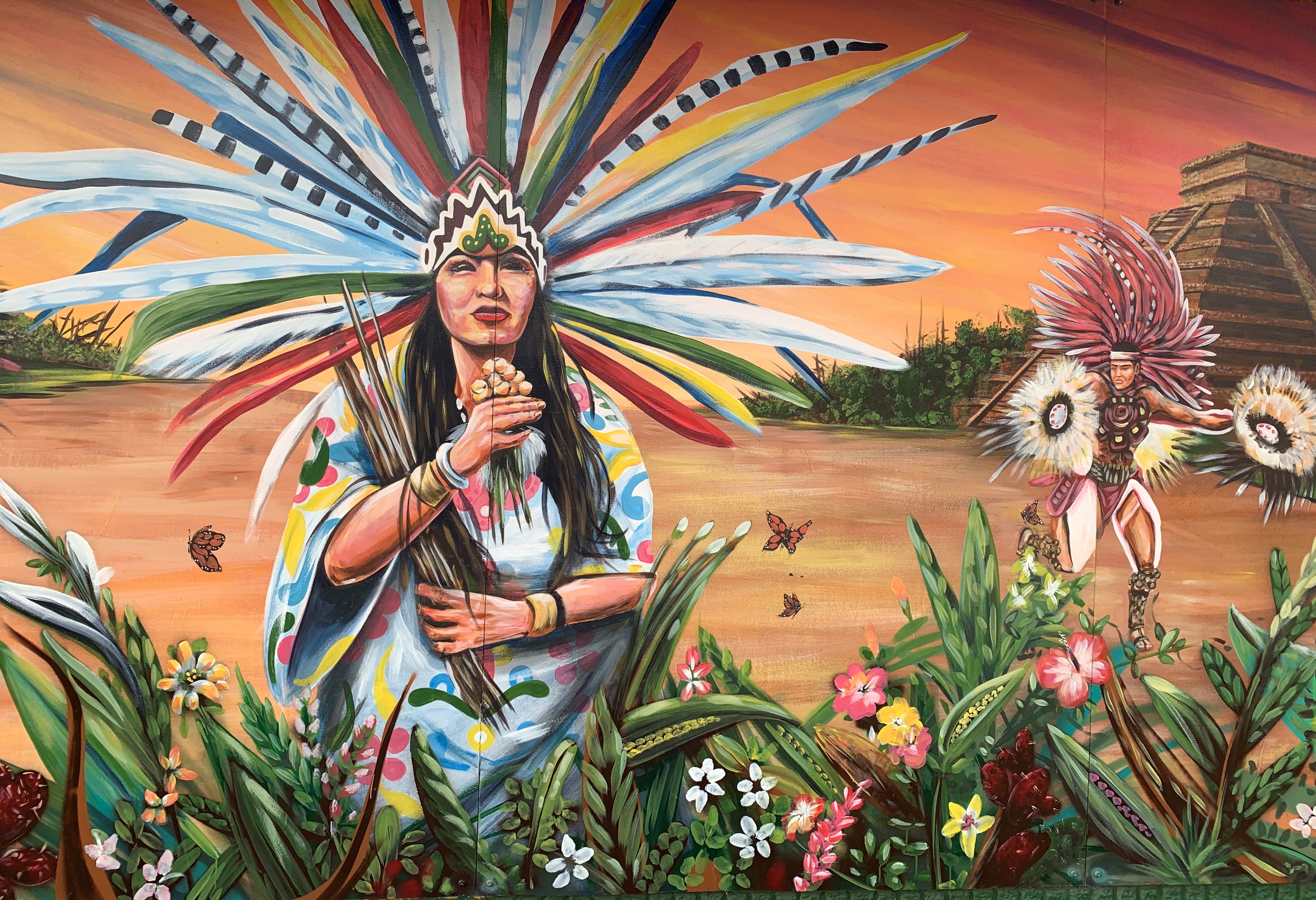 Un mural en East Chicago, Indiana, muestra a dos personas con ropas decoradas con largas y coloridas plumas, representativas de las culturas indígenas mexicanas, junto a mariposas monarcas.
