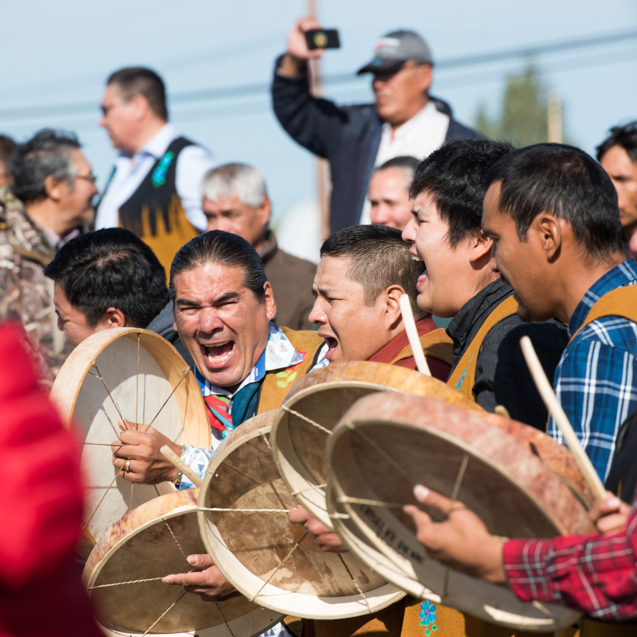 A group of eight men are yelling and beating drums