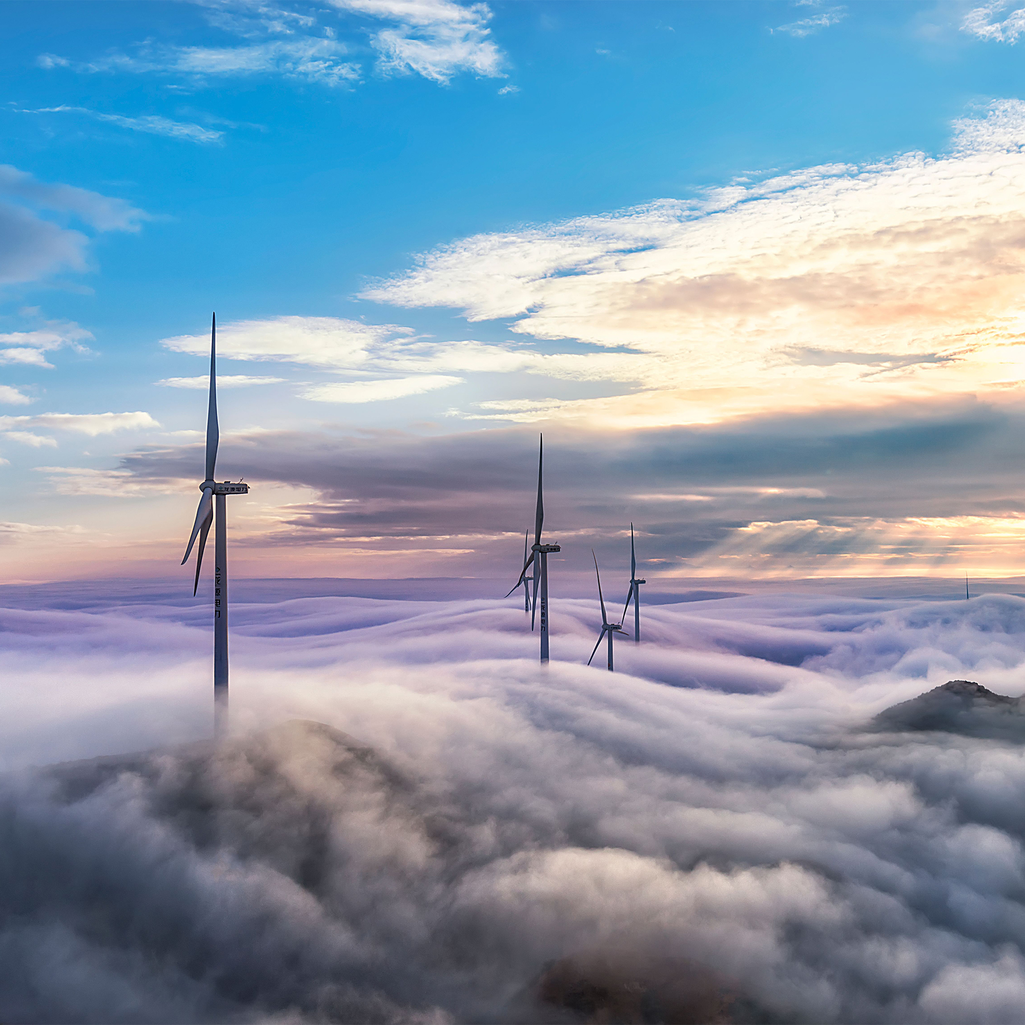 wind turbines poking up above low hanging clouds