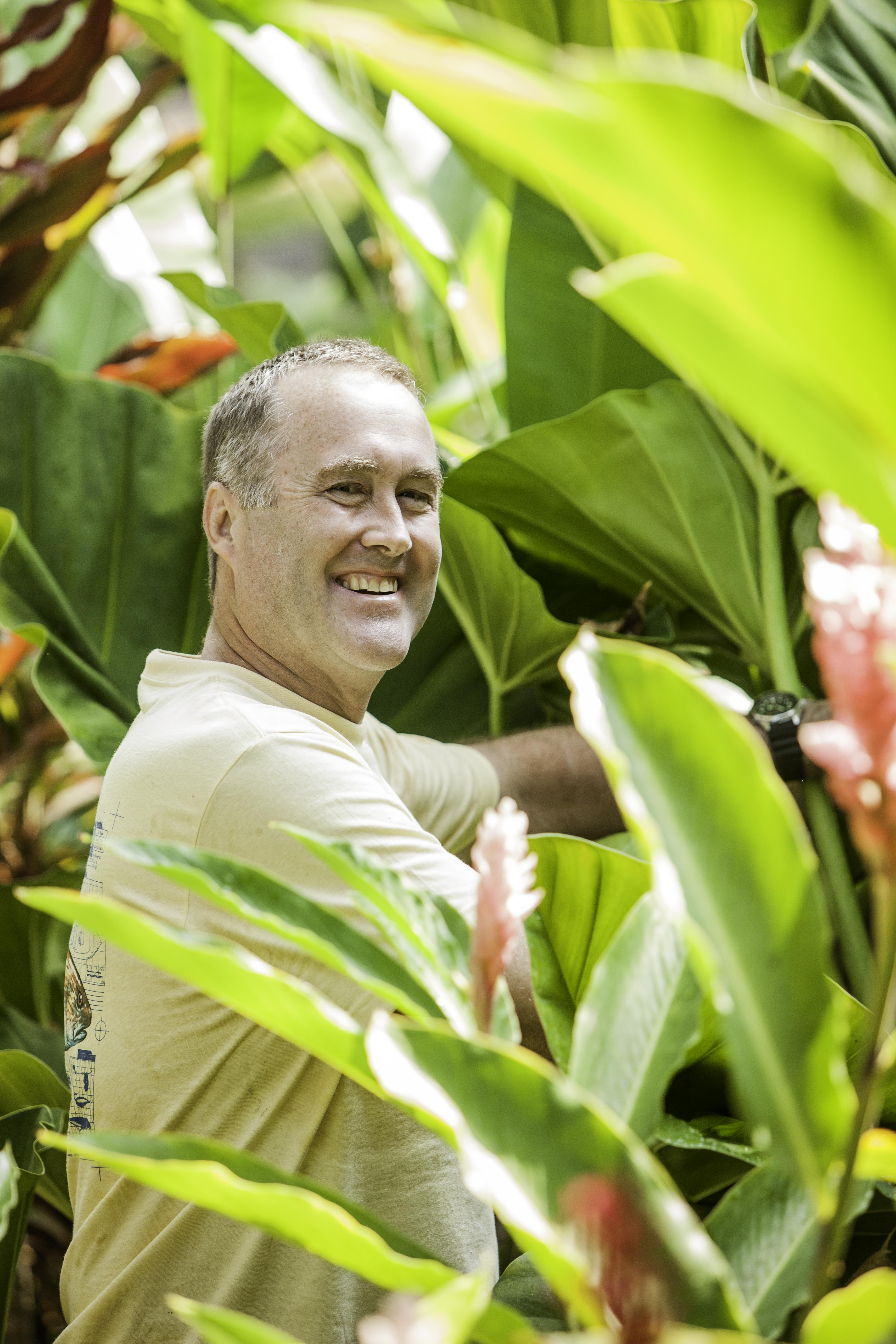 Bill Raynor stands in a tropical forest and smiles at the camera.