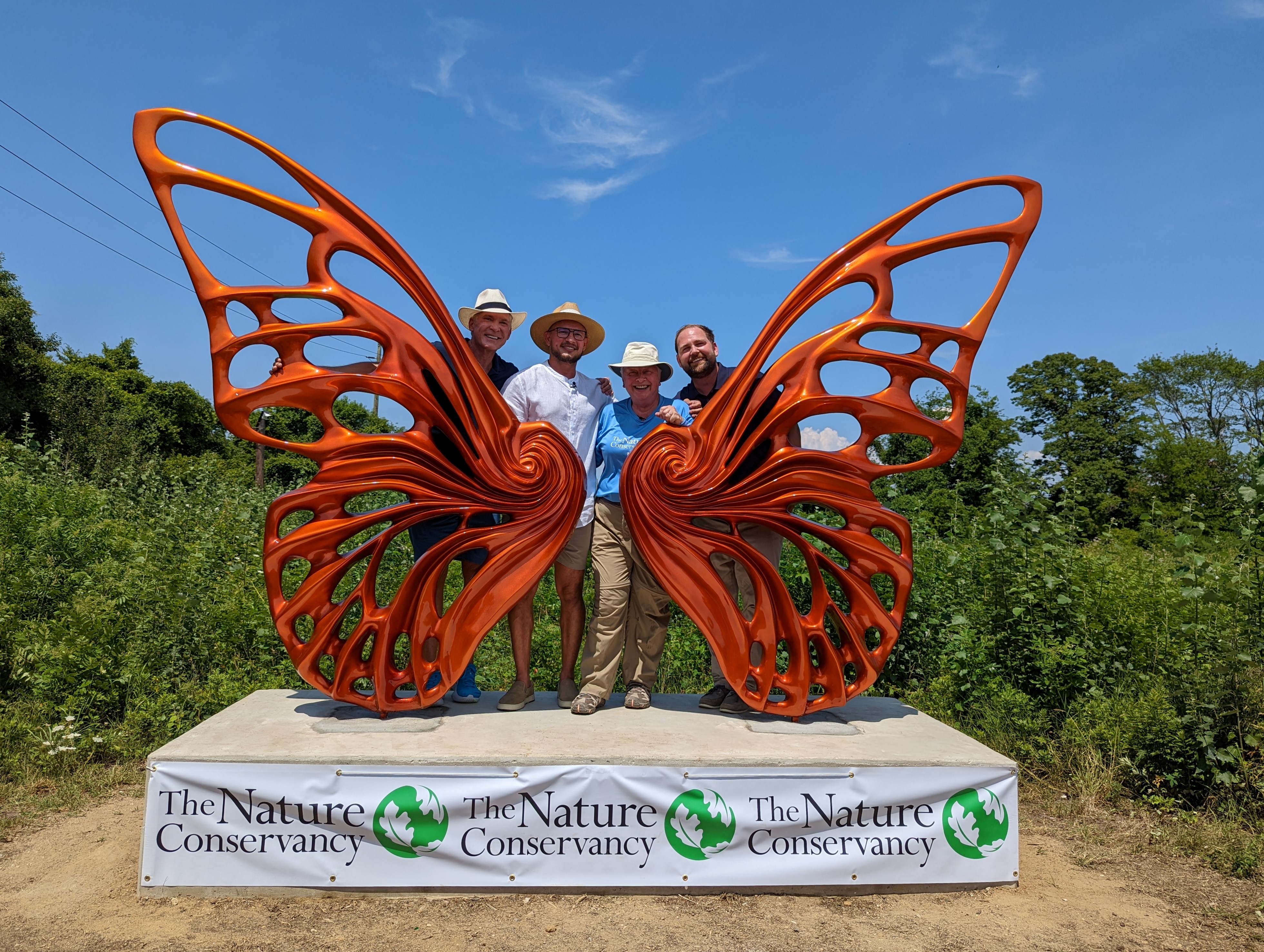 Four people are standing in front of a butterfly statue.