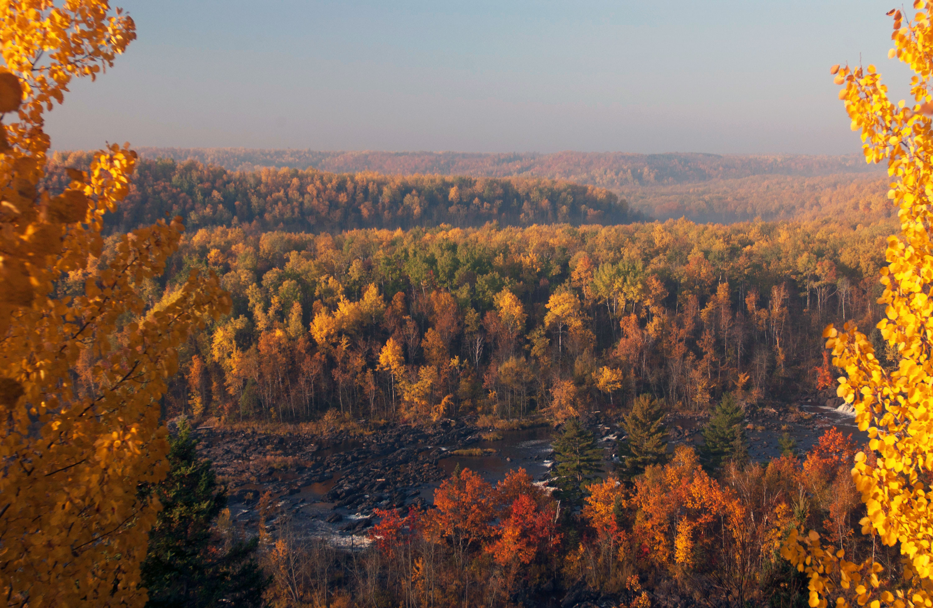 Brilliant autumn foliage on rolling ridges viewed from an elevated point with a rushing river below.