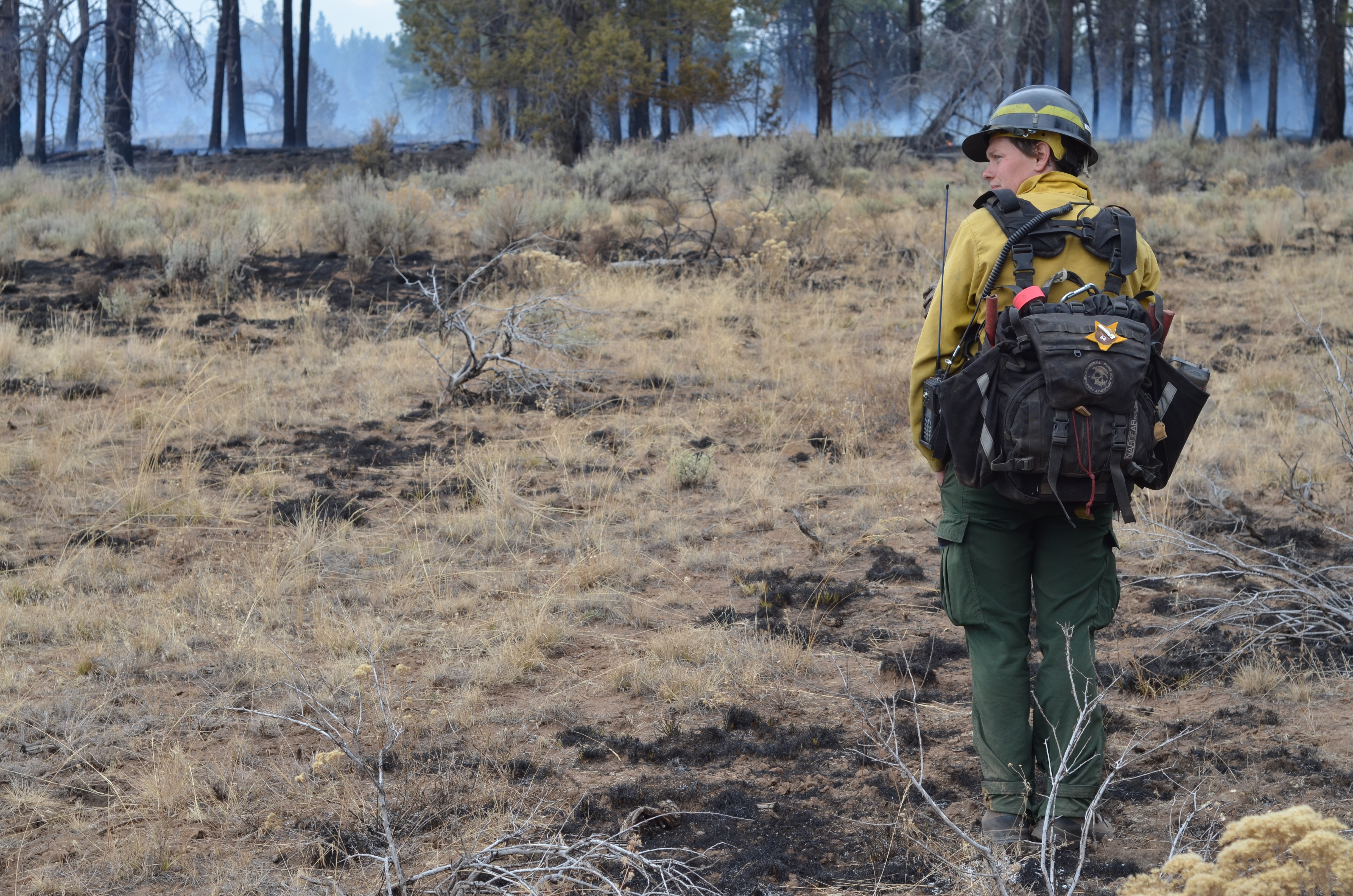 TNC Oregon Fire Manager Katie Sauerbrey stands in fire practitioner gear in front of a forest