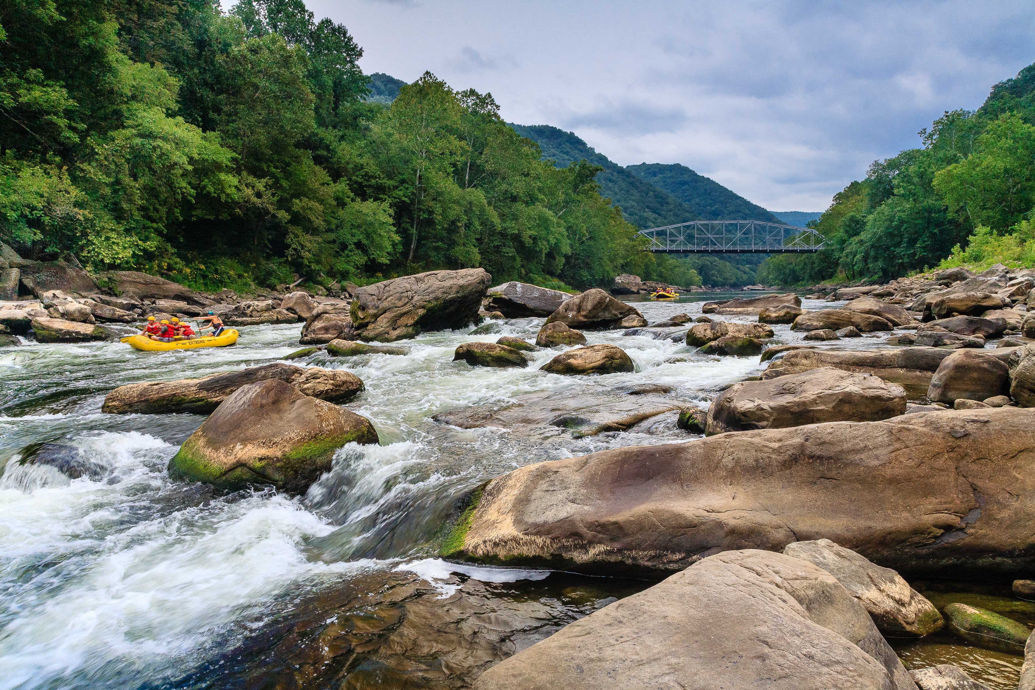 people in a whitewater raft exploring a rocky river with a bridge in the distance