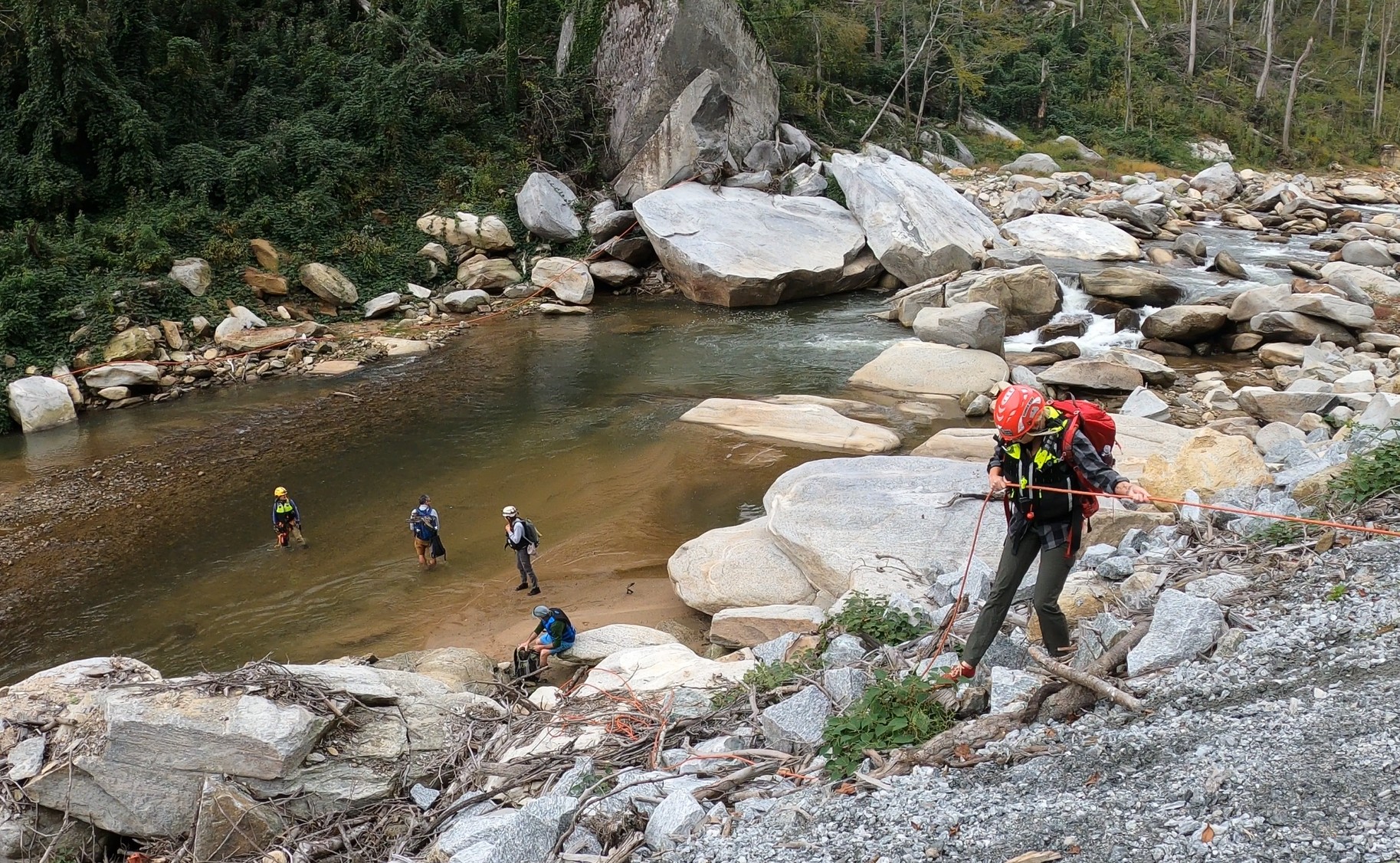 A group of people wearing life jackets and hard hats carefully cross over a river.