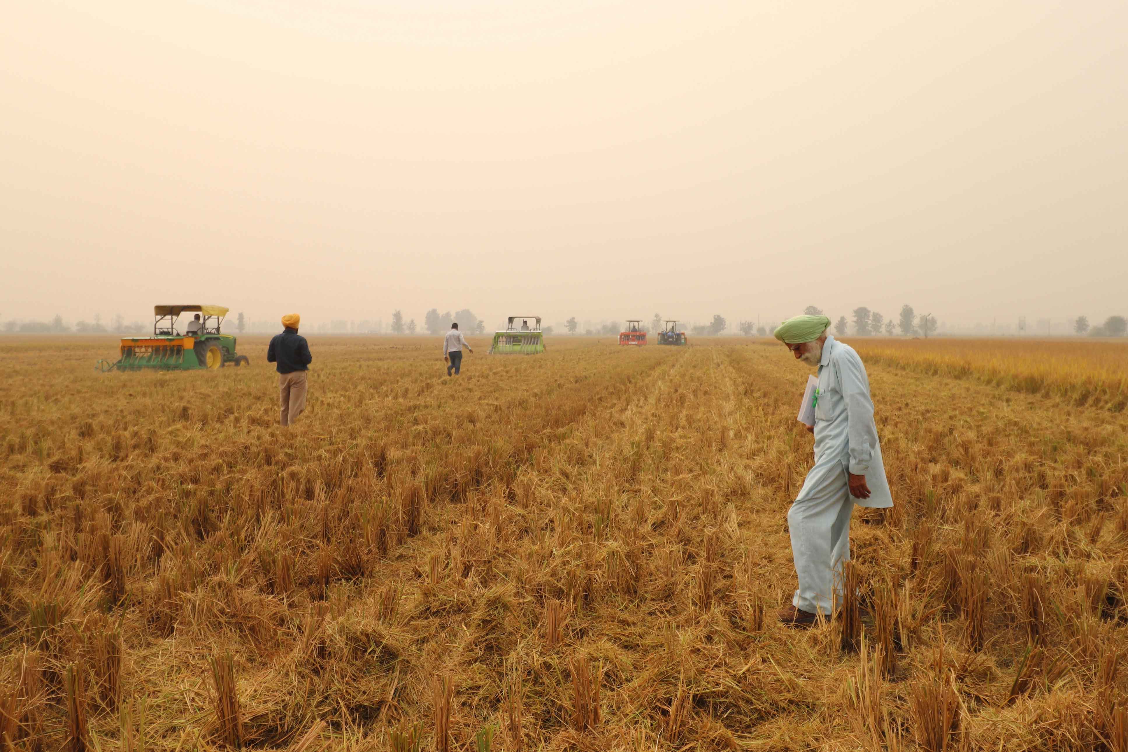 Farmers walk along crops while the sky is blanketed by opaque smog.