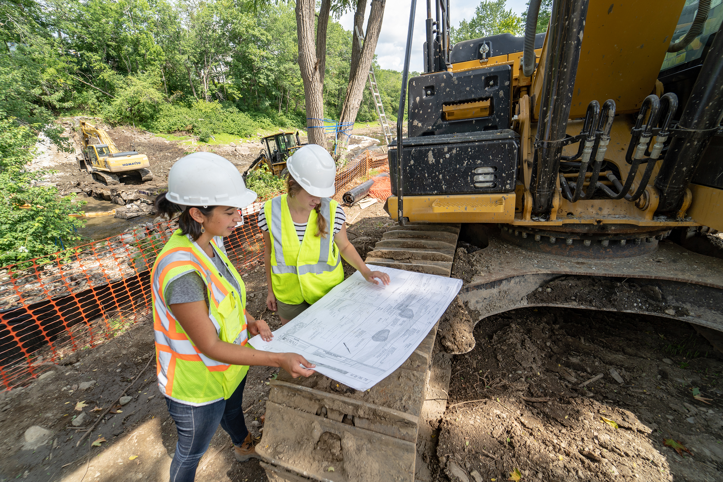 Two construction workers wearing hard hats examine a diagram.