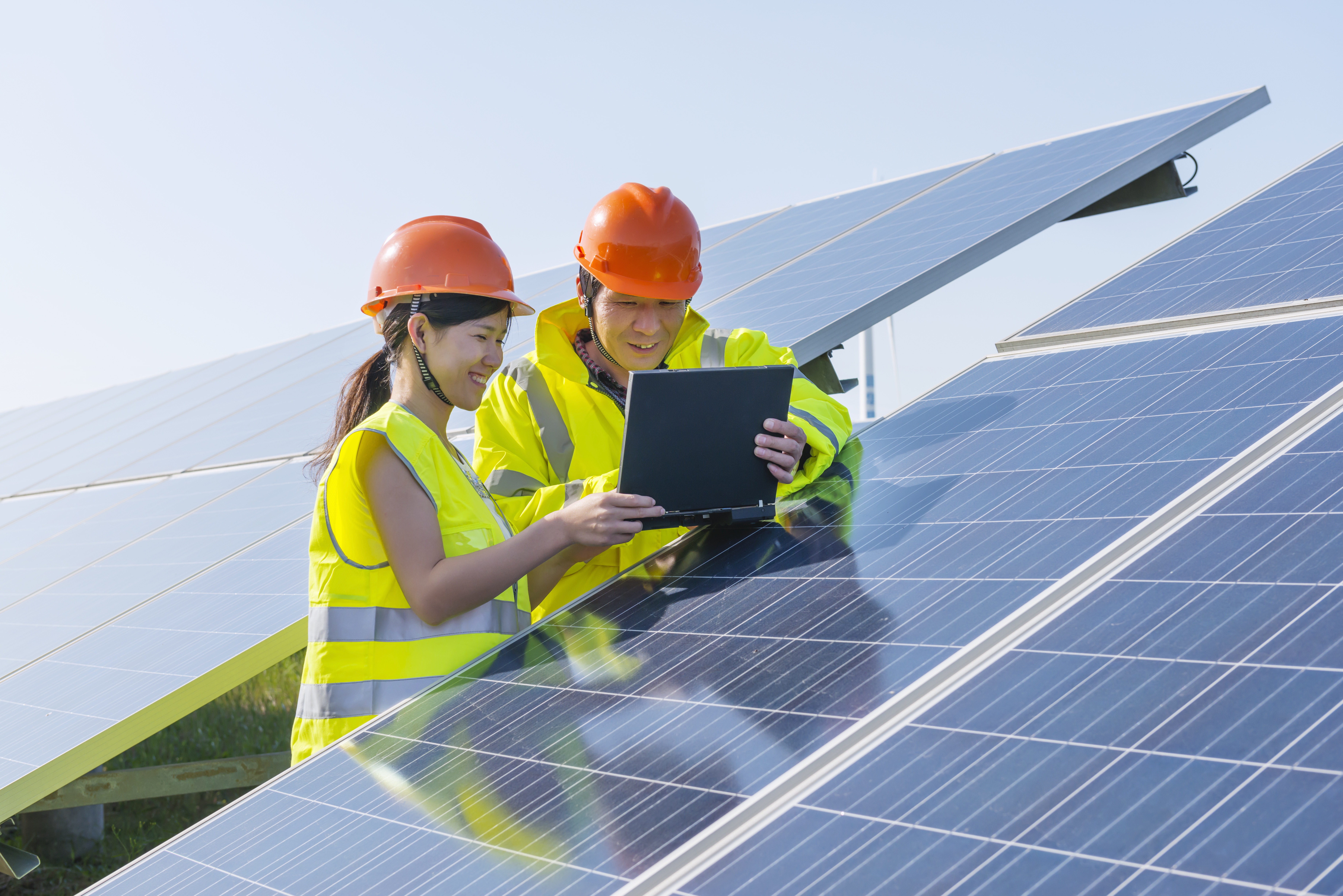 Two people in hard hats look at solar panels. 