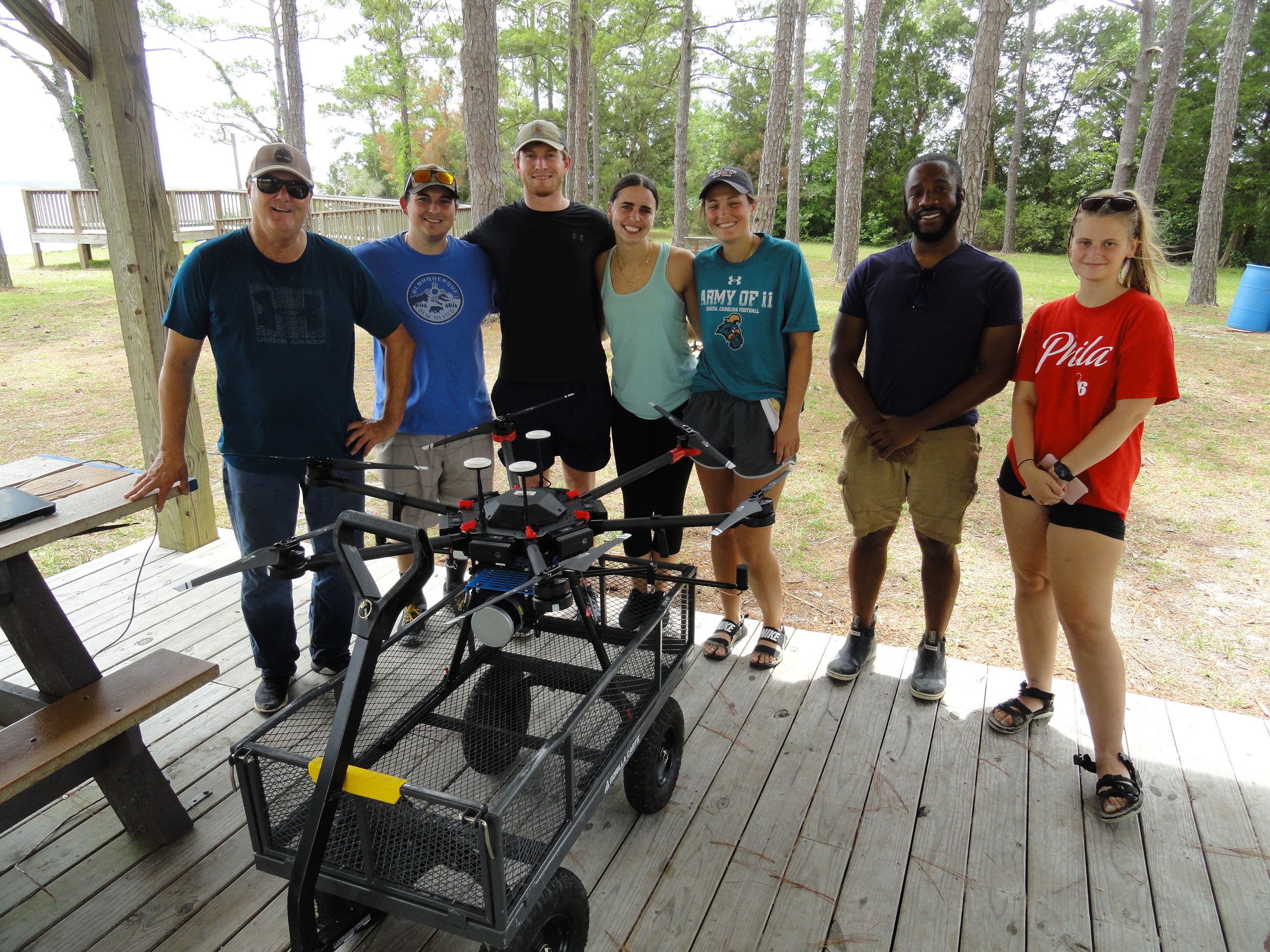 A group of seven college students pose around a drone. 