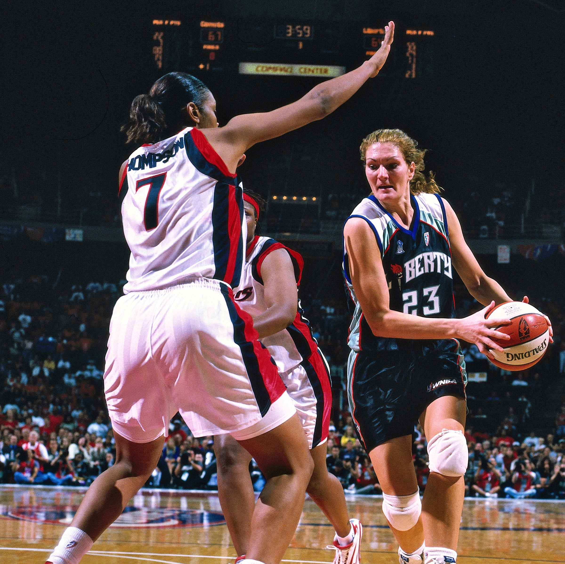 Woman in basketball uniform mid-game with basketball in hand on righthand part of screen.