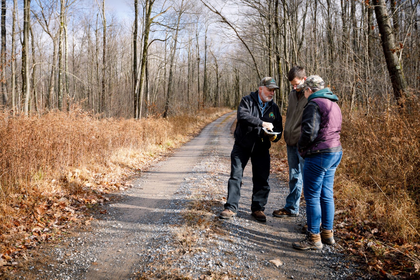 Three people stand together on the edge of a gravel road that extends into the horizon behind them.