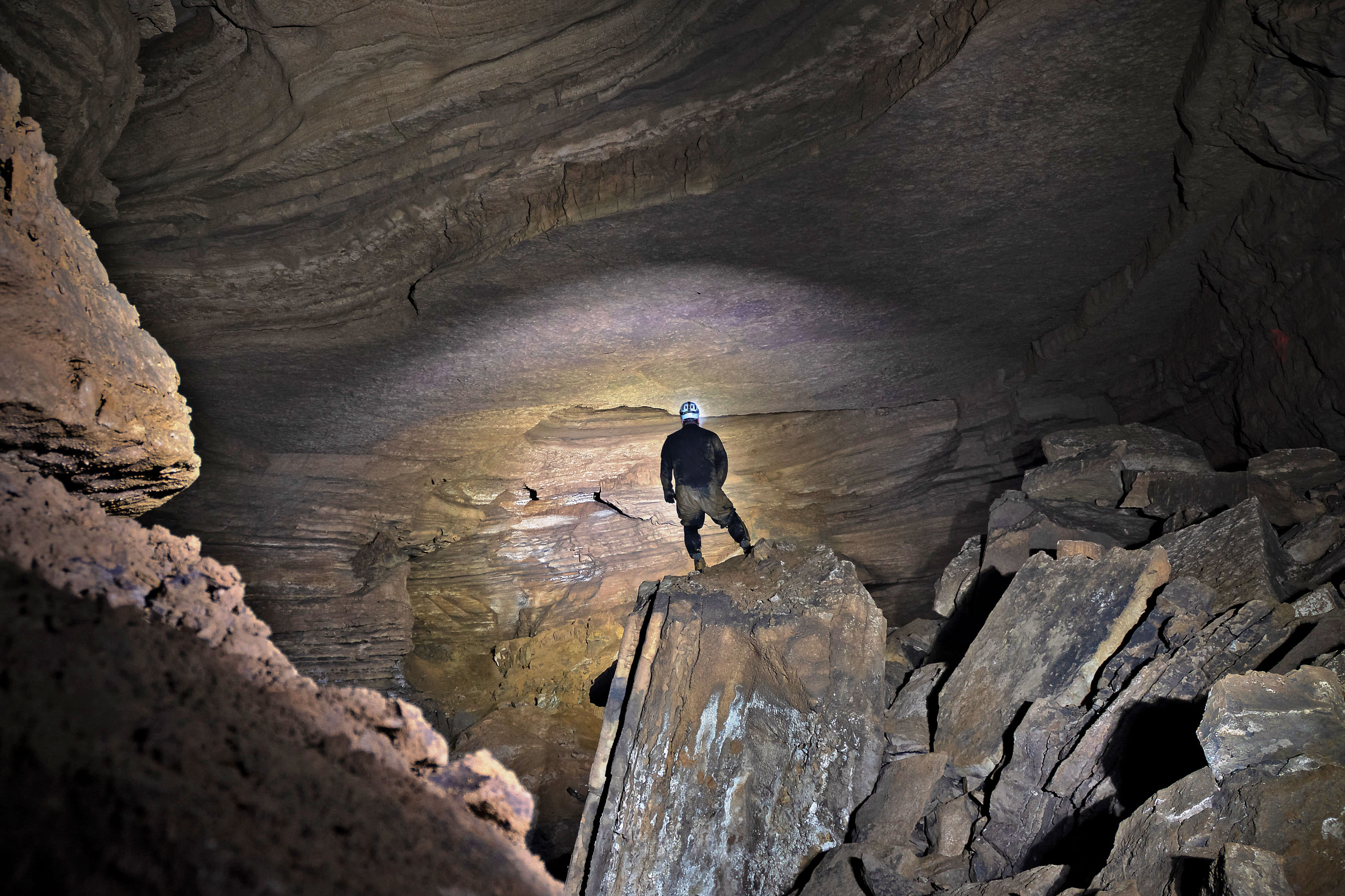 A man stands at the bottom of a large cave.