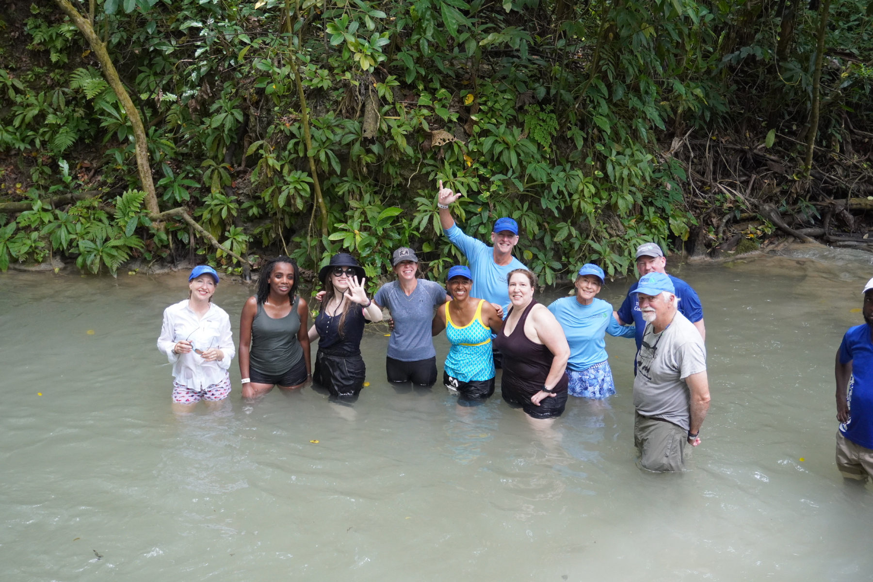 People stand waist deep in a freshwater stream in a Jamaican jungle.