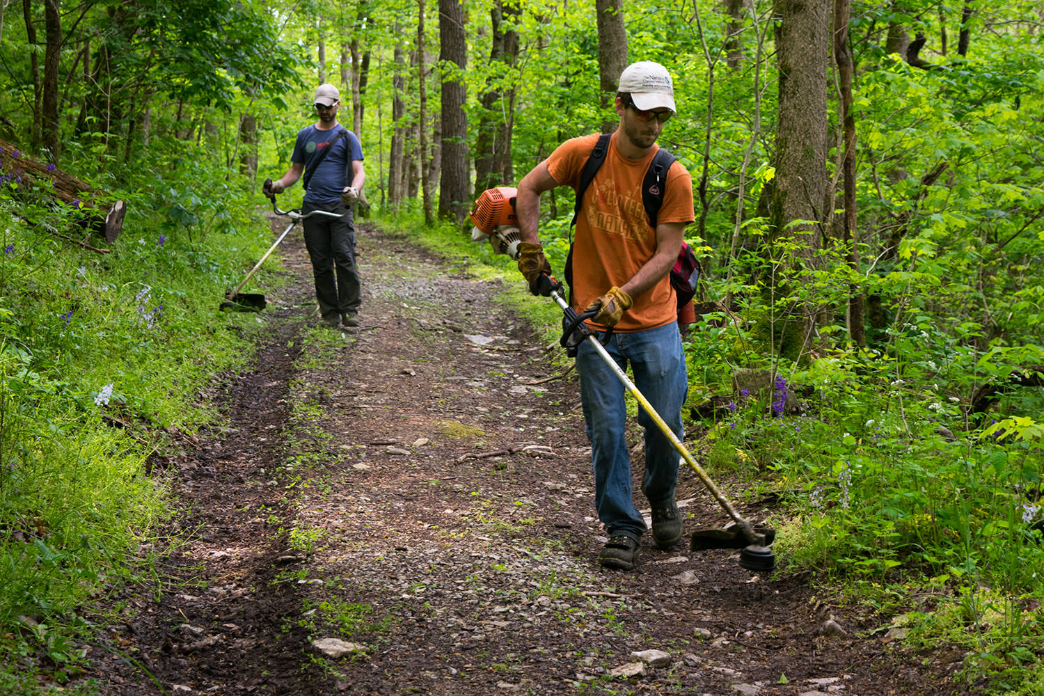 Two TNC employees use weed trimmers to clear a hiking trail.