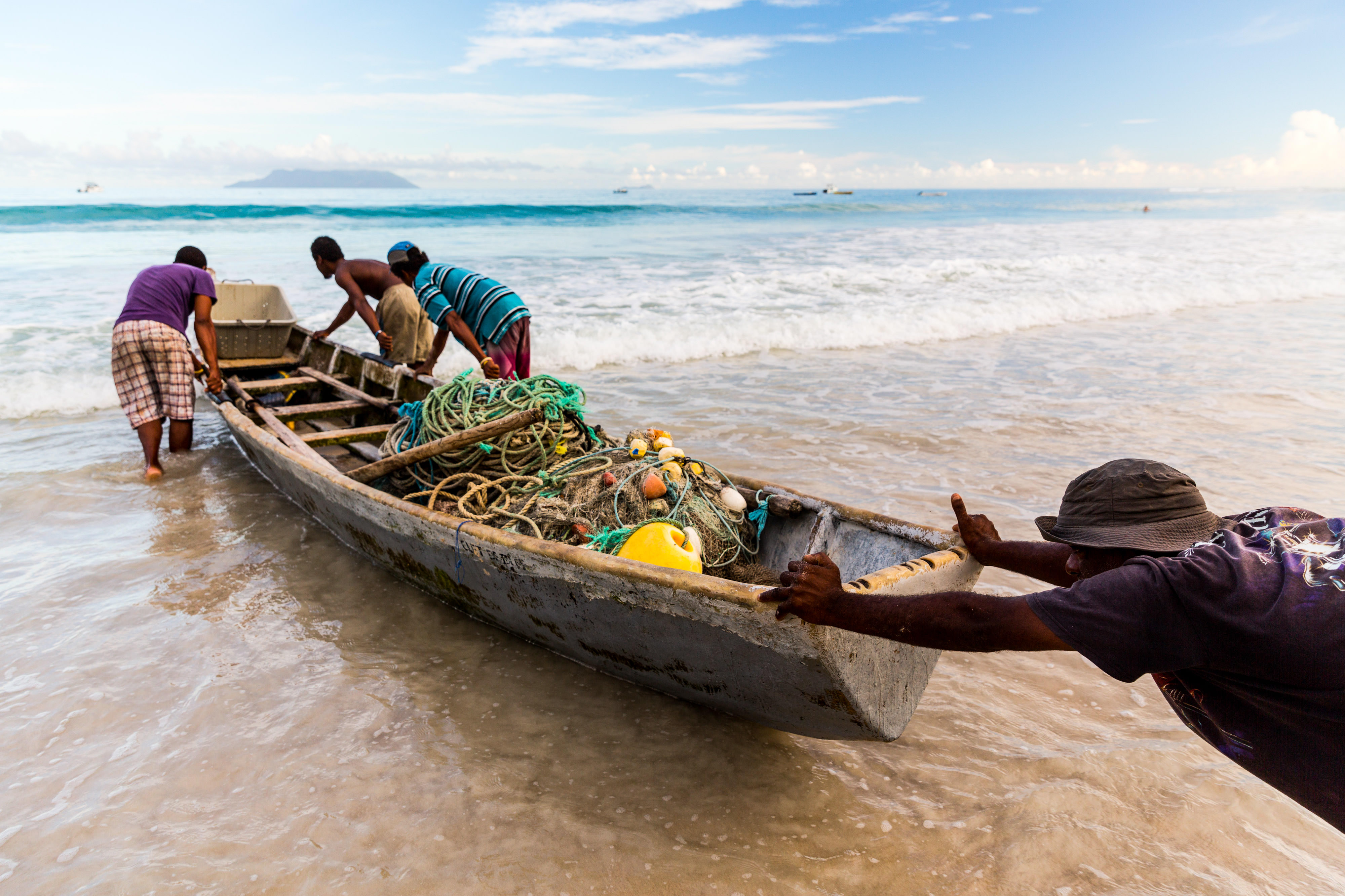 People pushing a small boat with fishing nets and gear through the waves into the sea.