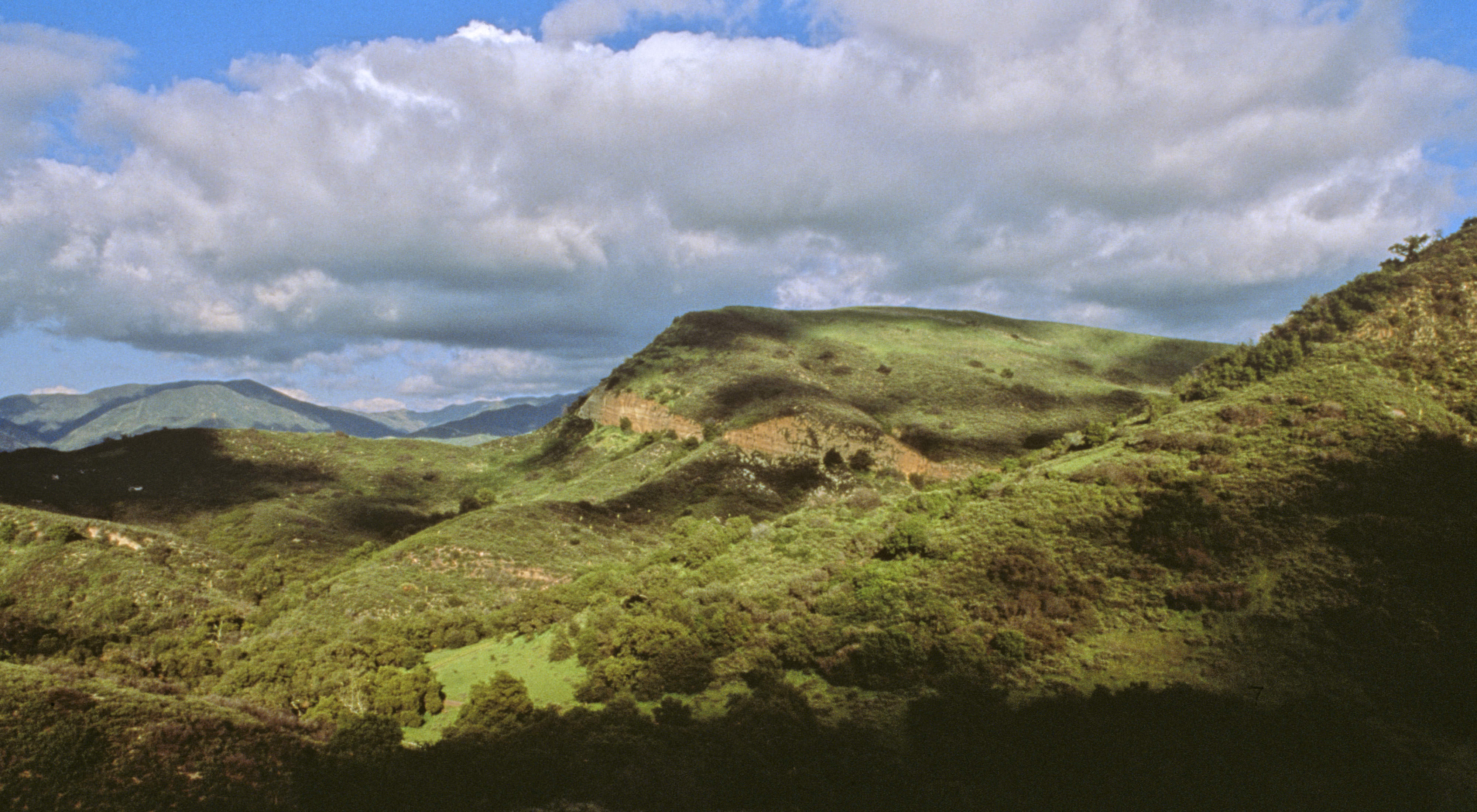 Dramatic shadows over grassy hills under a cloudy.