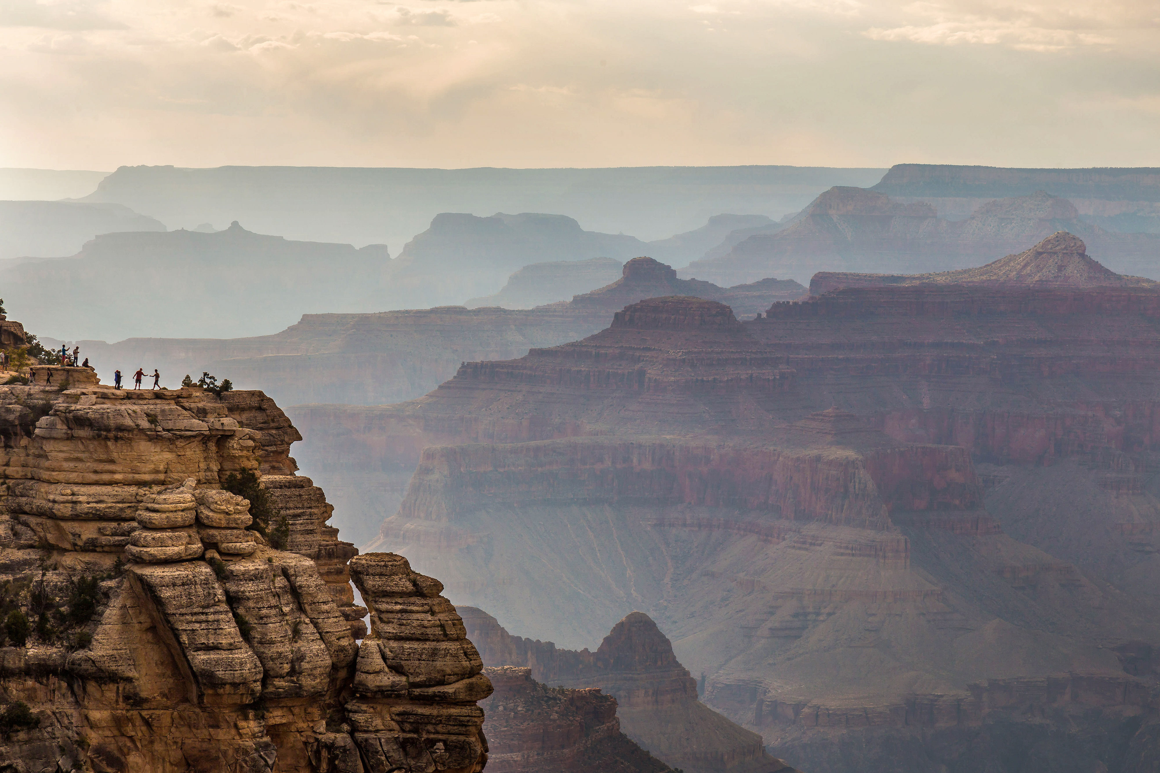 A few people stand atop a rock formation overlooking the Grand Canyon.
