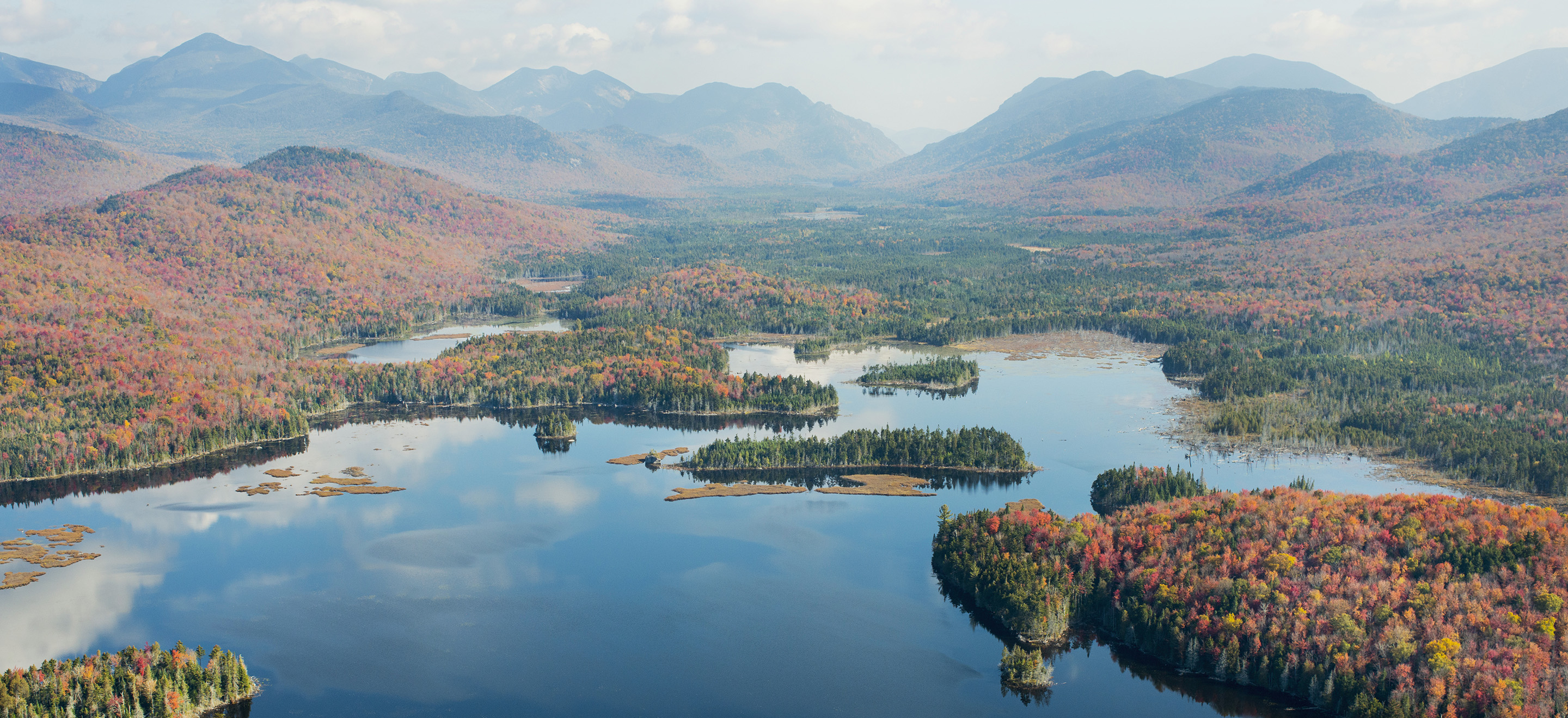 Aerial view of large pond surrounded by forested mountains.