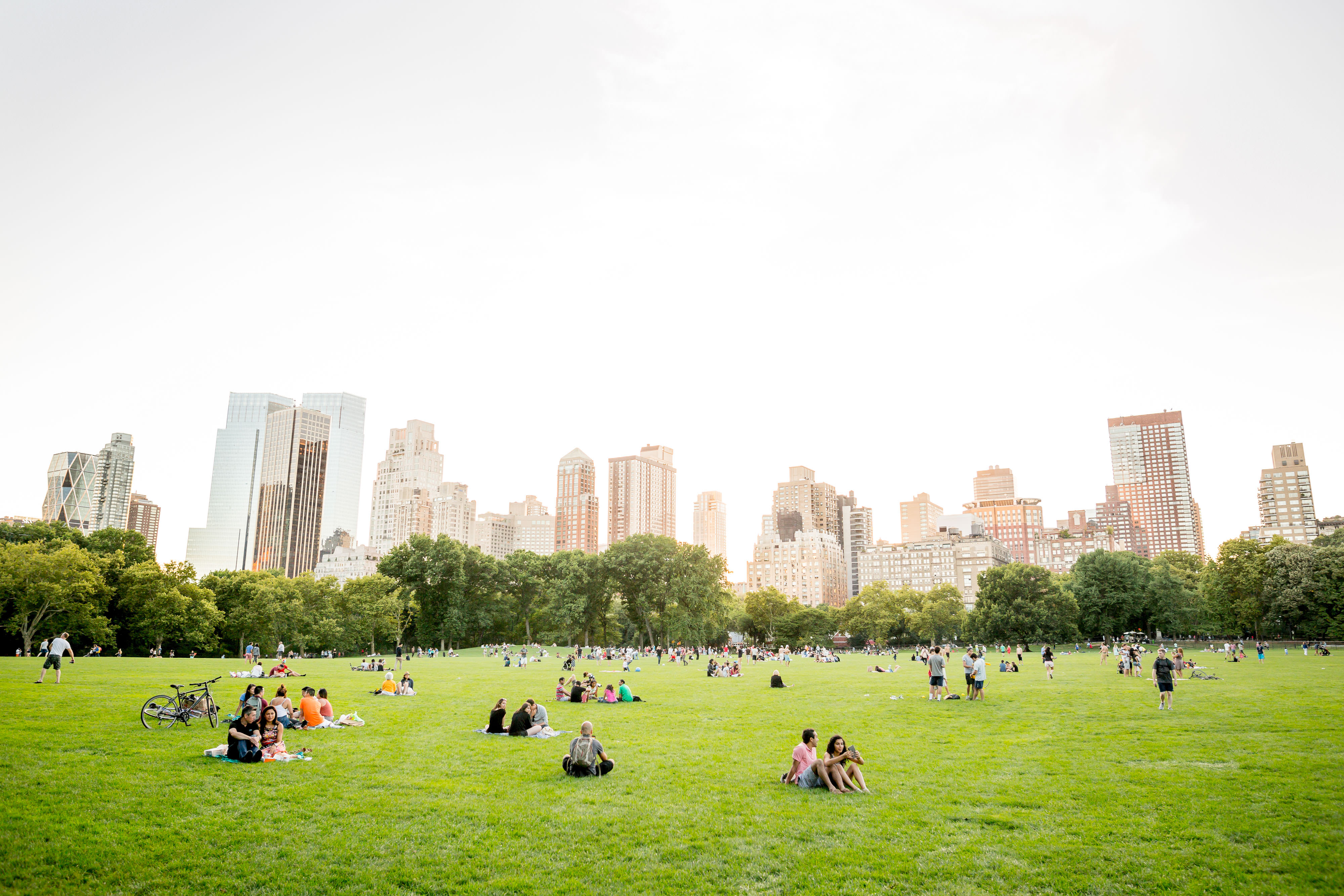 New York City skyline viewed from Central Park, where many people enjoy an open grassy field in the foreground.