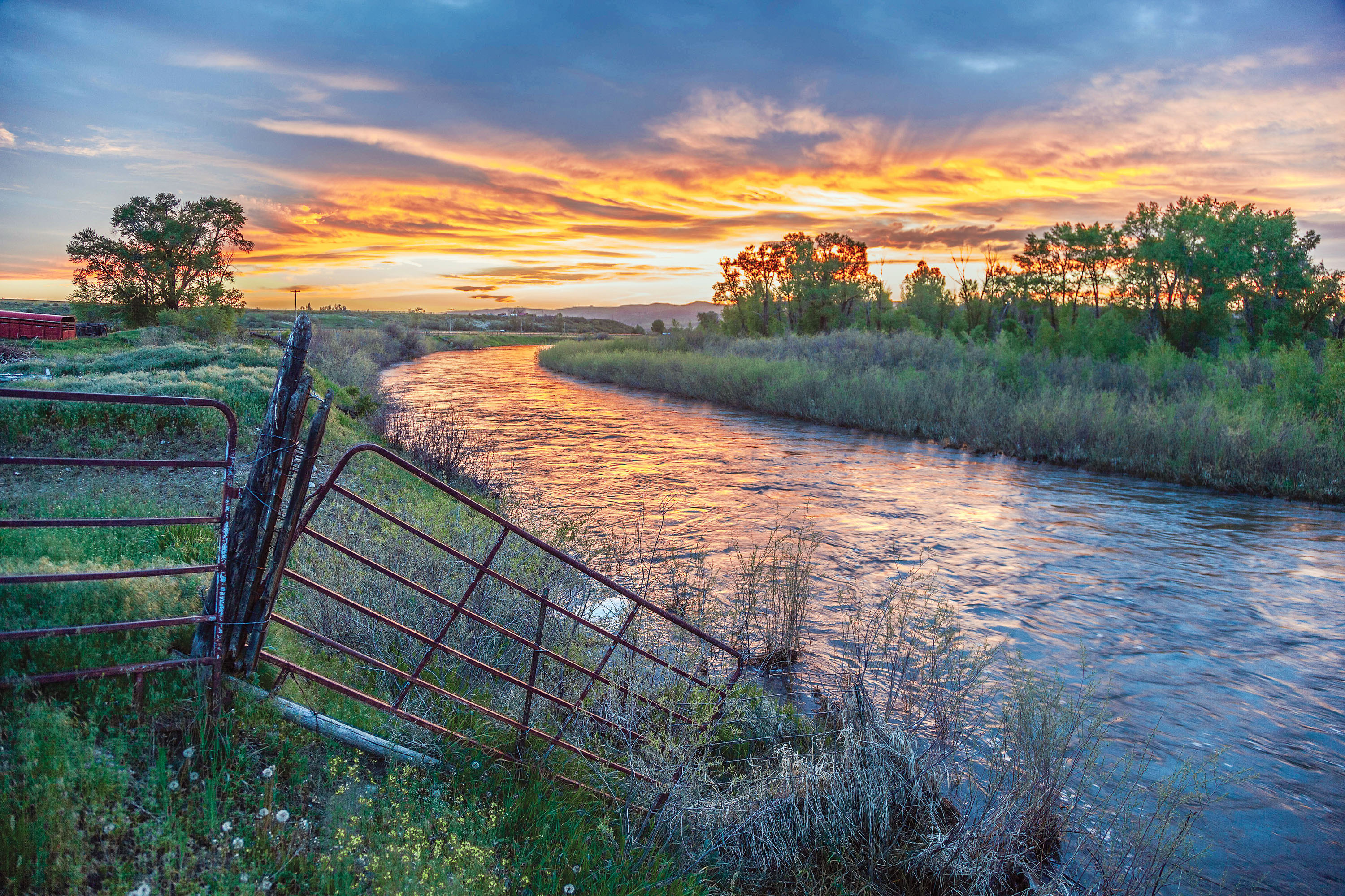A river flowing through marsh with a bright sunset reflecting on the river.