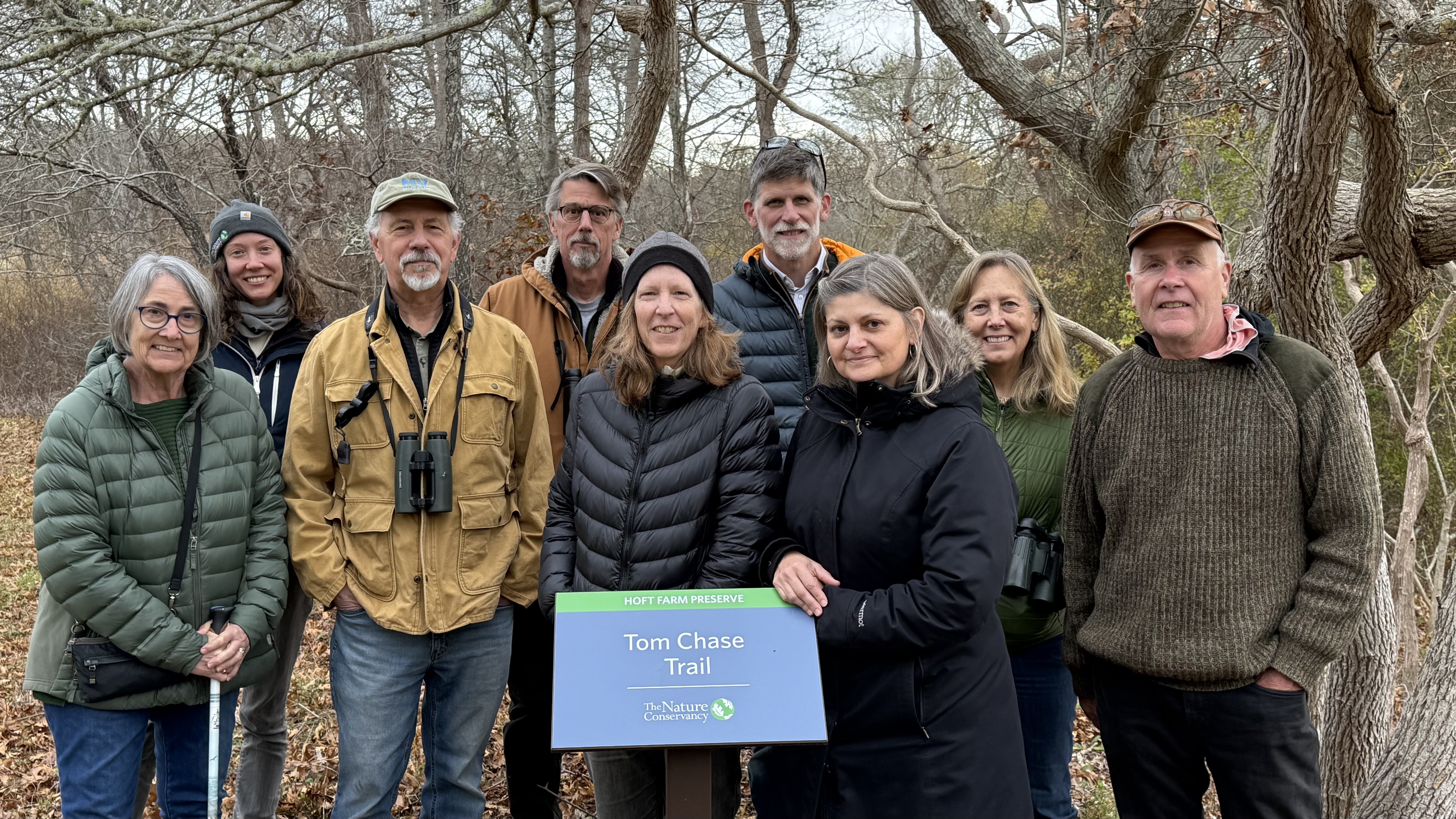A group of 8 men and women gather around a nature preserve sign. 