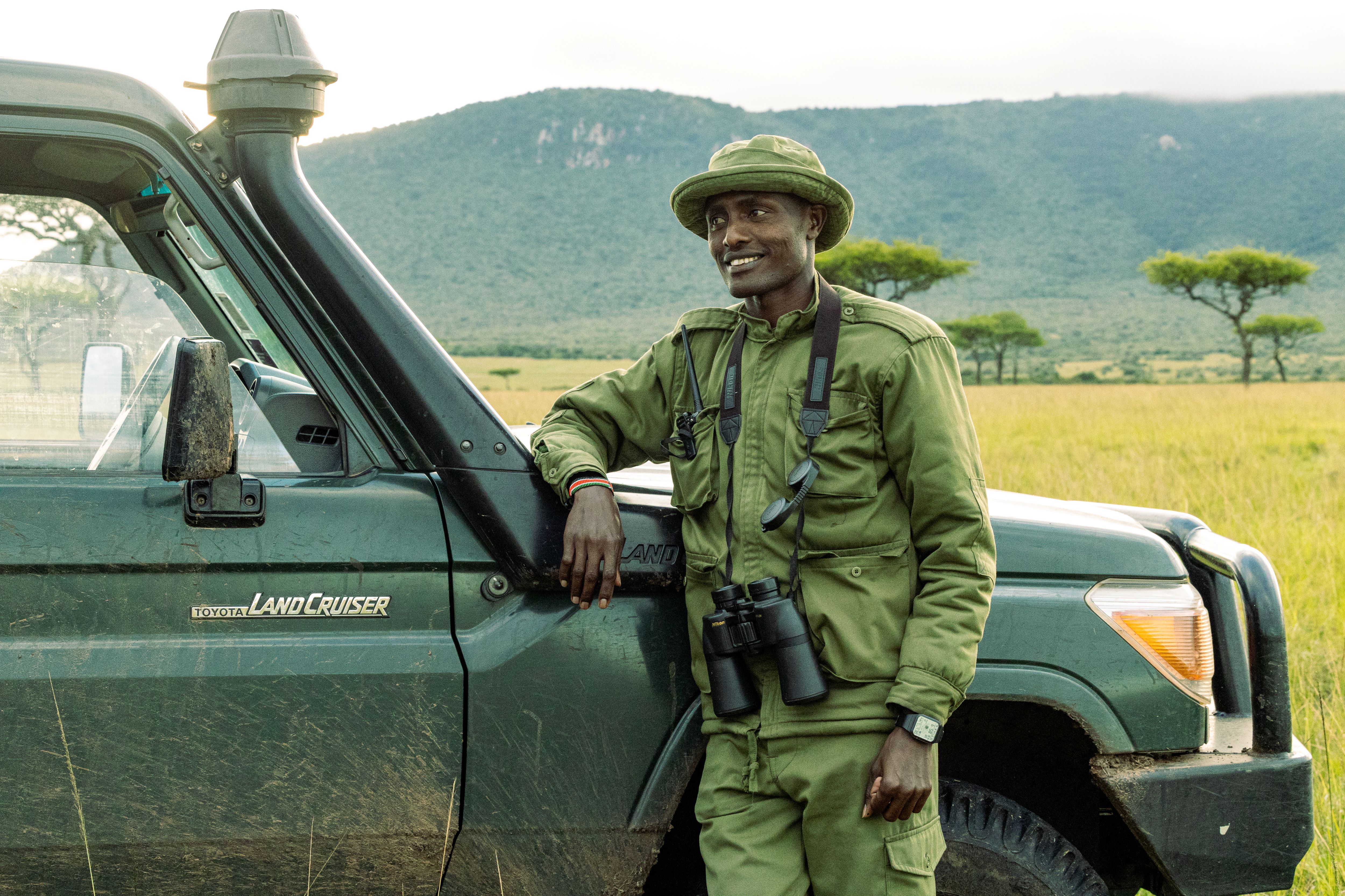 Tyson Nkurumua, dressed in ranger fatigues, stands and leans on his Land Cruiser. 