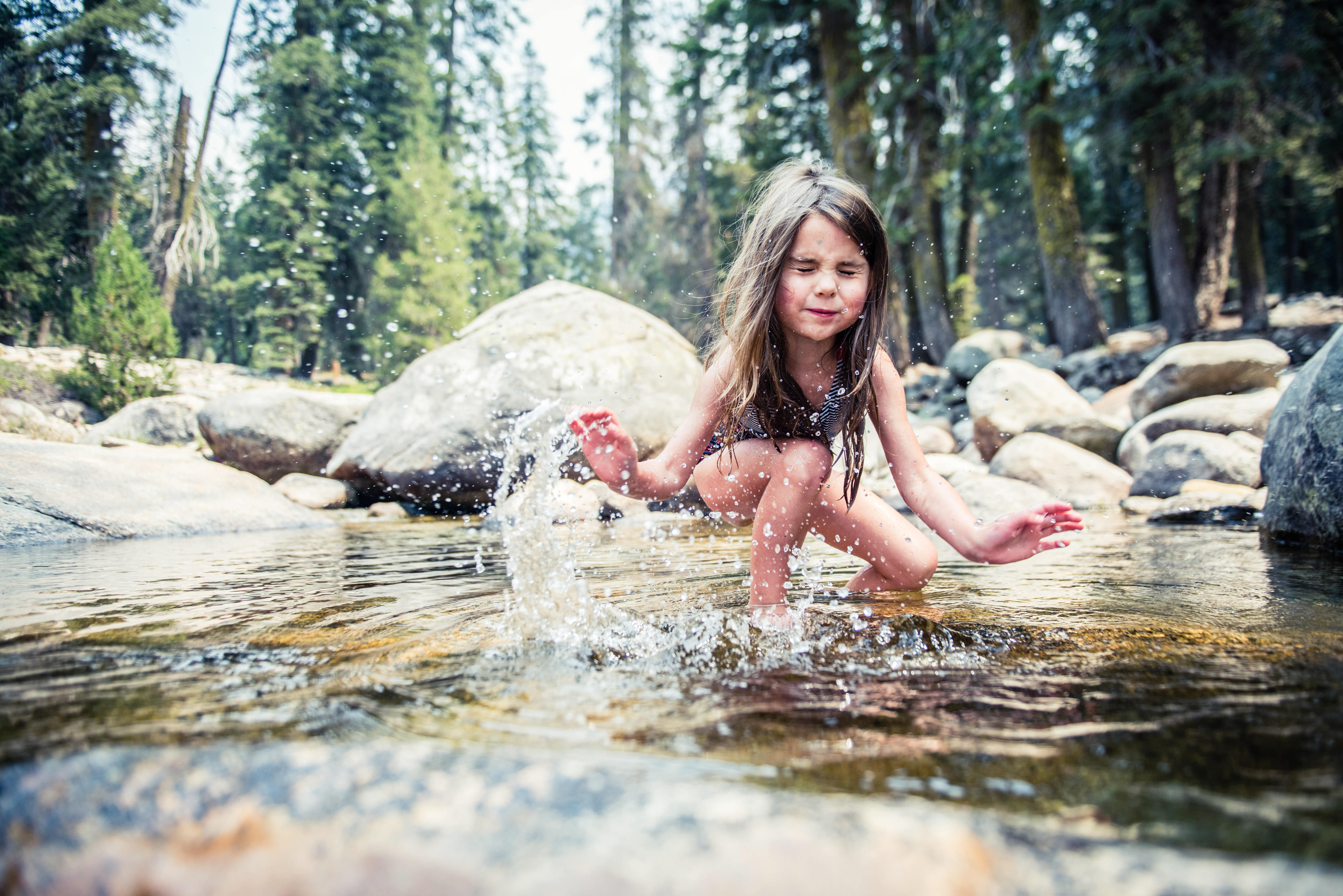 A girl splashes water in front of rocks.