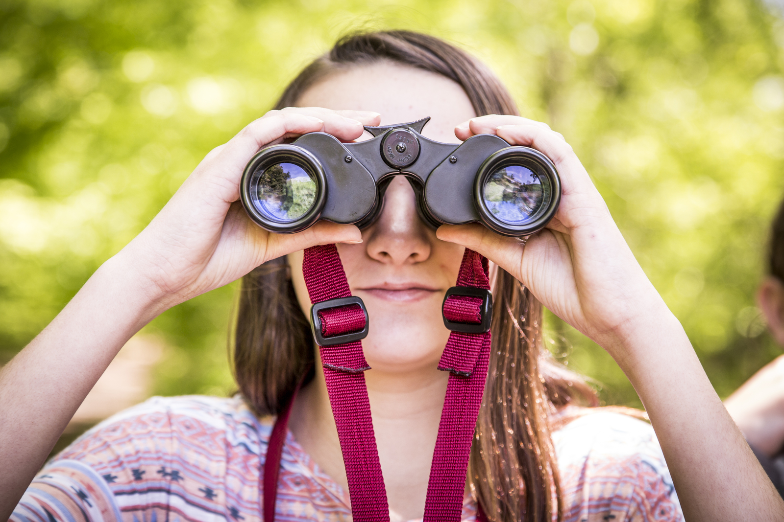 A young girl looks through binoculars directly at the camera.