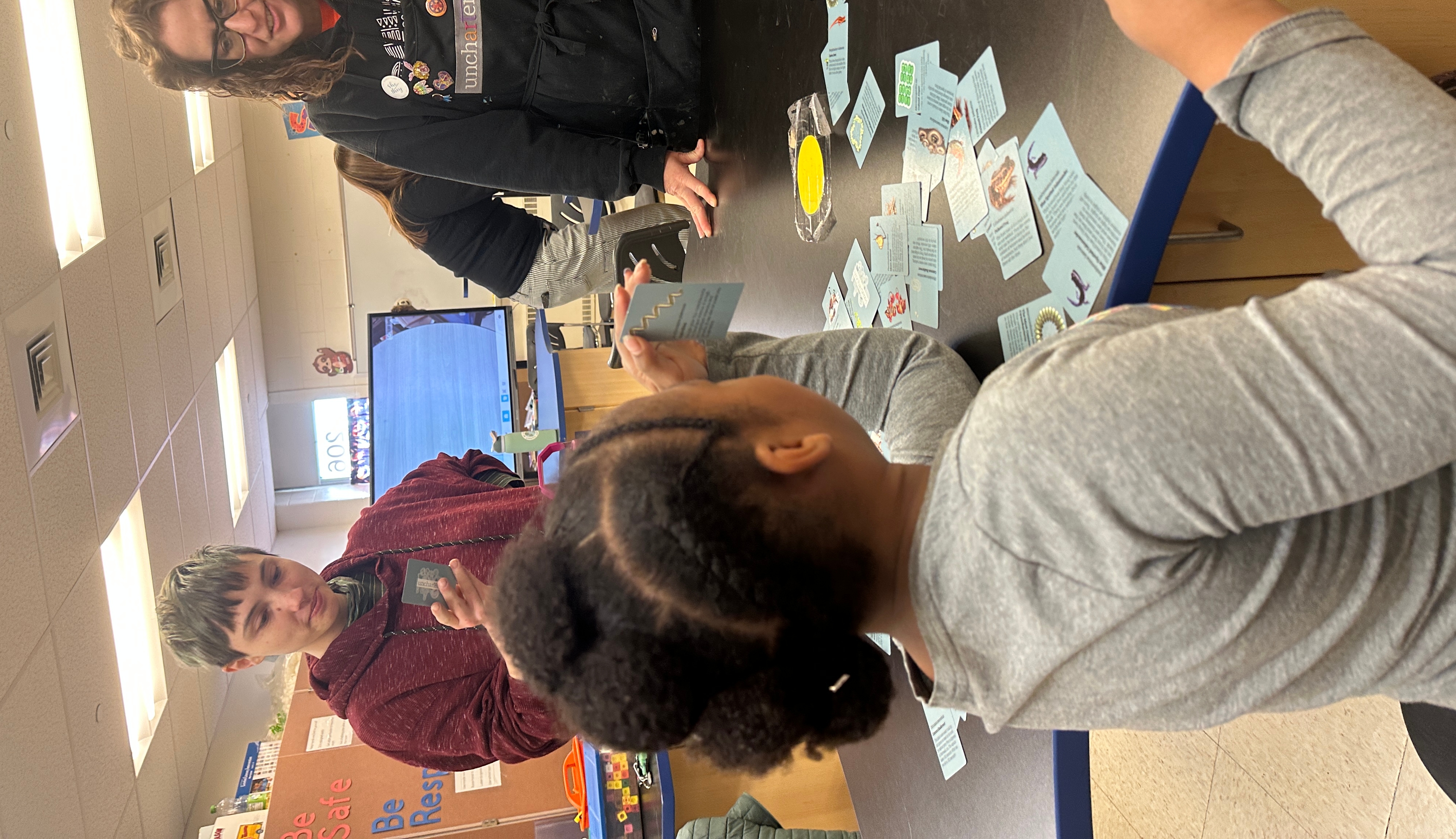 Children playing a card game while the teacher looks on.
