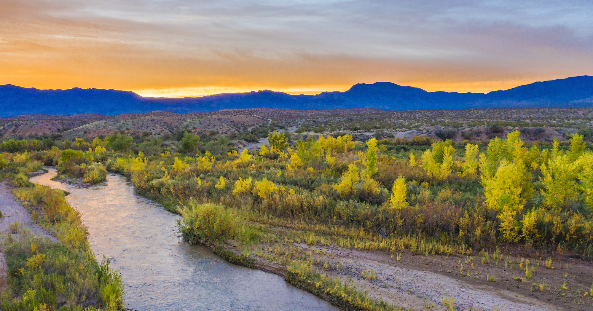 River flowing next to autumn color trees at sunset.