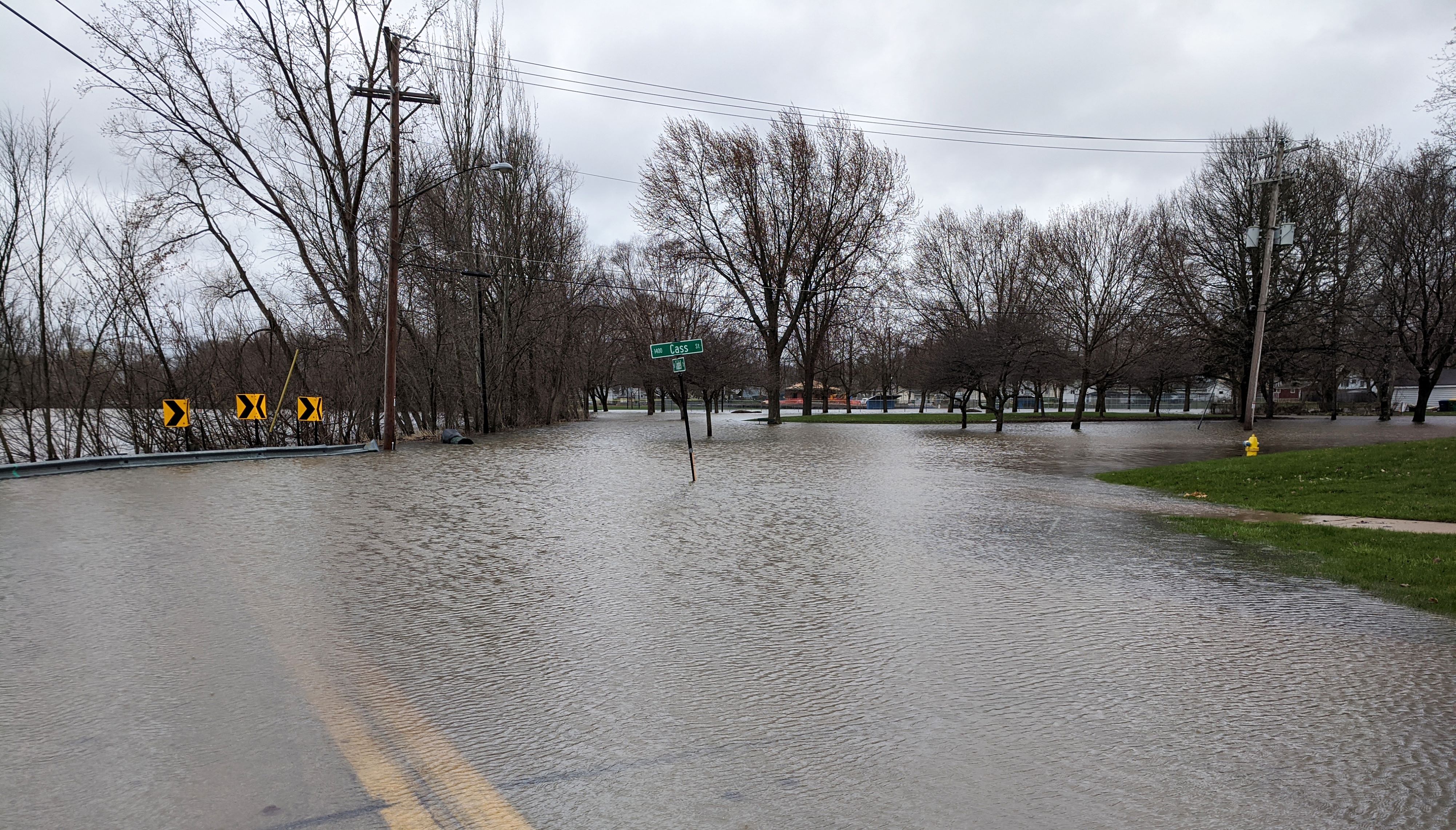 Flood waters cover a city roadway surrounding a post with green street signs.